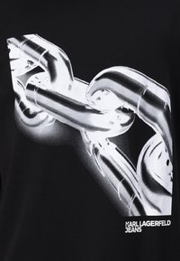 Juodas marškinėliai su stilizuota grafika, vaizduojančia sujungtus metalinius grandinės sidabrinės spalvos. Apačioje yra užrašas "KARL LAGERFELD JEANS".