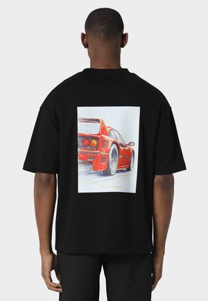 Mand iført sort T-shirt med en rød sportsvognsgrafik på ryggen, set bagfra mod en ensfarvet baggrund.