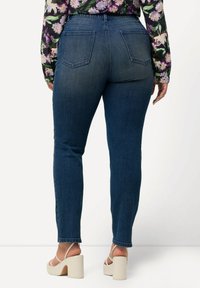 Tummansiniset skinny-farkut, joissa on sileä pinta, kaksi takataskua ja keskikorkea vyötärö. Yhdistetty kermaisiin alustakenkiin.