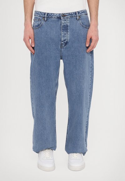 Modri jeans iz denima s sproščenim krojem, opremljeni z gumbnim zapiranjem, petimi žepi in z rahlimi zbledele. Nosi se jih z belimi supergami.
