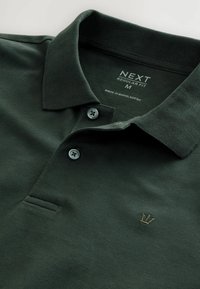 Dunkelgrünes Polo-Shirt aus strukturiertem Baumwollmaterial. Verfügt über einen klassischen Kragen, eine Knopfleiste mit zwei Knöpfen und ein kleines gesticktes Logo auf der Brust.