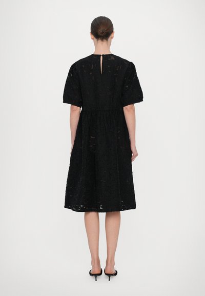Black lace dress with short puff sleeves, fitted waist, and a knee-length skirt. Features a small keyhole opening at the back.