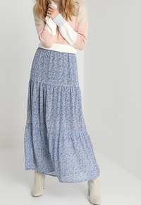 Pull en maille avec des rayures roses, blanches et bleues, associé à une longue jupe maxi à imprimé floral bleu et des bottines beige.