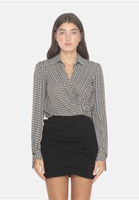 Blusa a maniche lunghe a fantasia bianca e nera con colletto, abbinata a una gonna a portafoglio nera aderente, con dettagli hardware minimi.