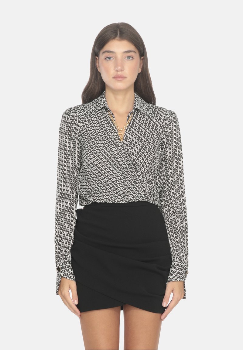 Blusa a maniche lunghe a fantasia bianca e nera con colletto, abbinata a una gonna a portafoglio nera aderente, con dettagli hardware minimi.