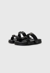 Svarte sandaletter med to brede spenn og spenne detaljer. Laget av glatt syntetisk materiale, med en polstret såle og flat design.