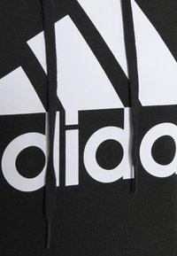 Felpa nera con logo "adidas" bianco. Presenta lacci con punte nere e un tessuto morbido e strutturato.