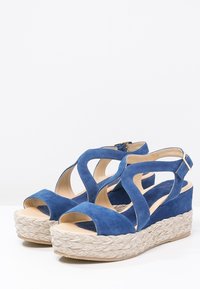 Sandali wedge in suede blu con suola in juta intrecciata, caratterizzati da motivi ritagliati e una fascia alla caviglia per supporto.