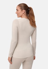 Lysebeige, tætsiddende langærmet top lavet af blødt stof, med rund halsudskæring og smalle ærmer, designet til komfort og lag-på-lag brug.