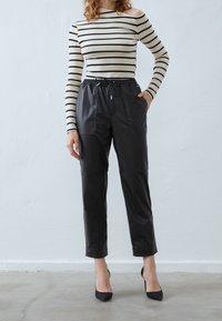 Pantalon court en cuir noir avec une taille à cordon de serrage et des poches latérales, associé à un haut rayé crème et noir à épaules dénudées.