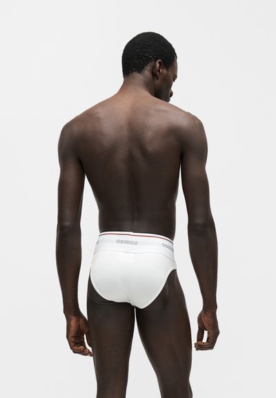 Άνδρας μοντέλο που φαίνεται από πίσω φοράει λευκά εσώρουχα DSQUARED2 σε απλό ανοιχτό γκρι φόντο.