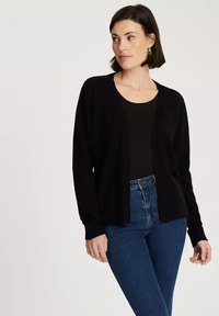 Czarny kardigan z otwartym przodem, długimi rękawami i miękką teksturą. Nosi się go na czarną bluzkę, w połączeniu z niebieskimi dżinsami z wysokim stanem.