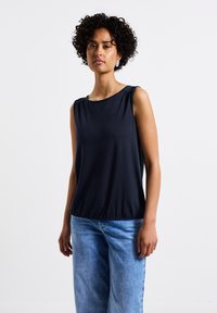 Ärmlös marinblå topp med avslappnad passform, rundad halsringning och subtila plisseringar vid axlarna. Kombinerad med ljusblå vida jeans.