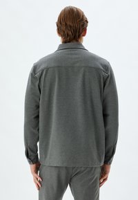 Grijze button-up shirt met een kraag, lange mouwen en een shirt-tail zoom. Heeft een gladde textuur en knoopdetails bij de manchet.
