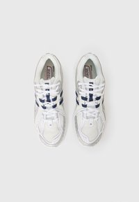 White athletic shoes with navy accents, mesh fabric, lace-up design, and a textured sole. Features a logo on the side and cushioned lining.