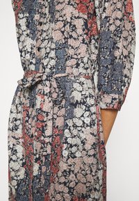 Abito floreale di color blu scuro, con fiori rosa, rossi e bianchi. Maniche lunghe, chiusura a bottoni e una cintura legata in vita.