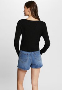 Top nero a maniche lunghe con righe abbinato a pantaloni corti di denim blu; presenta un collo a barchetta e una vestibilità aderente, che mette in evidenza il dettaglio sul retro.