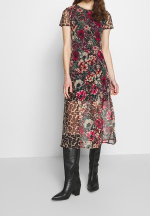 Femme portant une robe mi-longue à manches courtes avec des motifs floraux et léopard, associée à des bottes en cuir noires montant jusqu'aux genoux.