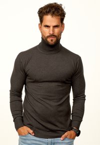 Dunkelgrauer Rollkragenpullover in einem taillierten Design. Mit gerippten Bündchen und Kragen. Getragen mit hellblauen Jeans. Hohe Textur.