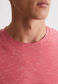 Czerwony T-shirt w paski z okrągłym dekoltem. Materiał wydaje się miękki o subtelnej fakturze, z naprzemiennie jasnymi i ciemnymi czerwonymi paskami.