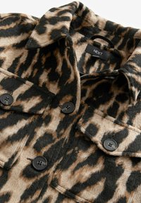 Leopard-tulostettu takki vaaleanruskeassa ja mustassa värissä. Valmistettu pehmeästä huopamateriaalista, jossa on kaksi rintataskua ja mustat napit.