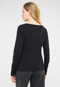 Czarna bluzka z długim rękawem wykonana z miękkiego materiału, z szerokim dekoltem i subtelnym logo z tyłu. Połączona z czarnymi jeansami w panterkę.