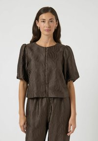 Brun tekstureret top med puffærmer, der har et bølgemønster og rund halsudskæring, båret med matchende bukser. Glat stof, afslappet design.