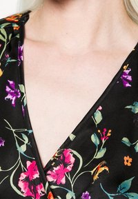 Blommönstrad svart tyg med rosa, lila och gula blommor, med en djup v-ringning och mjuk, slät textur.