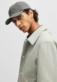 Gray cotton baseball cap with curved brim, worn with light gray woolen coat featuring a structured collar and button closures.