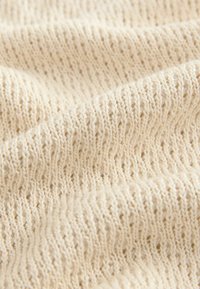 Beige strikket stof med en fin ribbet tekstur, der har jævnt fordelte masker og et blødt, let udseende.