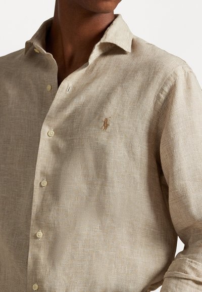 Chemise beige à carreaux avec un col, dotée de petits boutons et d'un logo brodé discret sur la poitrine gauche. Tissu texturé.