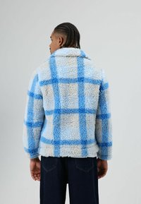 Blue and cream plaid sherpa jacket with a collar and textured surface, featuring blue grid patterns and a relaxed fit.