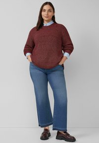 Winiakowy sweter dzianinowy z okrągłym dekoltem, połączony z jasnoniebieską koszulą z kołnierzykiem oraz szerokimi niebieskimi dżinsami. Ciemne loafersy dopełniają stylizację.