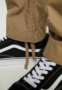 Mustat kangastennarit valkoisilla yksityiskohdilla ja nauhoilla, yhdistettynä khakinvärisiin housuihin, joissa on teksturoidusta kankaasta valmistettu ja nilkasta kapeneva malli.