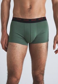 Grüne Boxershorts aus weichem Stoff mit einem schwarzen Bund, der "HUGO" in roter Schrift zeigt, entworfen für eine enge Passform.