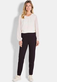 Lichte, vloeiende crème blouse met een samengetrokken halslijn, gecombineerd met op maat gemaakte zwarte broeken en witte sneakers. Zacht materiaal en slim-fit ontwerp.