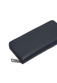 Granatowy portfel ze skóry o fakturowanej powierzchni, zamykany na suwak, z subtelnym logo. Kompaktowy, prostokątny kształt z trwałymi elementami metalowymi.