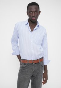 Φωτεινό μπλε πουκάμισο με ρίγες και κουμπιά, με μια τσέπη στο στήθος, σε συνδυασμό με γκρι τζιν και καφέ δερμάτινη ζώνη.