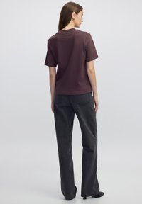 Camiseta marrón de manga corta combinada con jeans de pierna ancha en gris oscuro. La tela parece suave y el ajuste es relajado. Elementos de diseño simples.