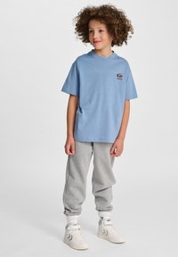 Jasnoniebieska bawełniana koszulka z krótkim rękawem i małym wyszywanym logo, w połączeniu z szarymi dresami i białymi trampkami za kostkę.