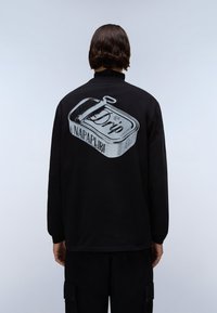 Fekete pulóver, amelyen egy lehúzós konzerv grafikája és a "Drip" valamint a "NAPAPIJRI" felirat szürkében található a hátoldalon.