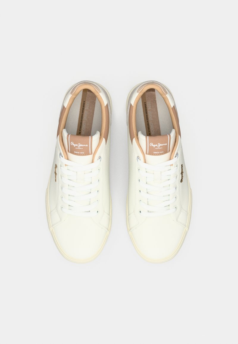 Un par de zapatillas blancas de corte bajo con acentos beiges, cordones blancos y etiquetas de marca en la lengüeta, mostradas desde una vista superior sobre un fondo blanco.