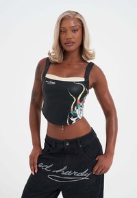 Top corto negro con gráficos florales y un acento crema en el escote, combinado con pantalones de mezclilla oscuros que presentan un estampado de logo.