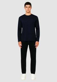 Camicia a maniche lunghe blu navy con scollatura rotonda, abbinata a pantaloni neri e sneakers bianche. Tessuto liscio, design aderente, dettagli minimi.