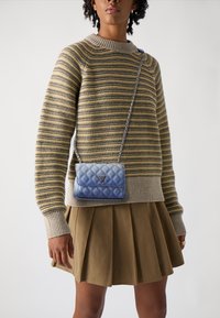 Borsa a tracolla blu trapuntata con una catena argentata, indossata sopra un maglione a righe, abbinata a una gonna plissettata color khaki.