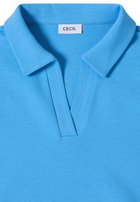 Lyseblå polo-shirt med fladt krave og V-udskæring. Har et mærke med "CECIL"-label. Lavet af blødt, glat stof.
