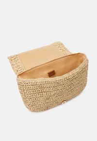 Borsa di paglia intrecciata beige con un interno liscio color cuoio. Presenta un bordo frangiato e una chiusura a bottone a pressione per un accesso sicuro.