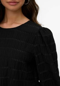 Zwarte textuur top met verticale plooien en subtiele horizontale strepen, met een ronde halslijn en puffed mouwen.
