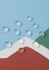 Kapi vode na teksturiranoj tkanini. Pozadina sadrži svijetloplave, zelene i crvene geometrijske oblike s glatkom završnom obradom.