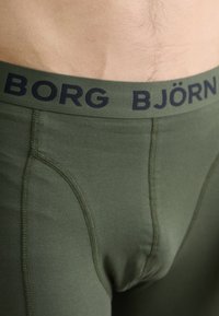 Olive green elastic boxer briefs featuring a navy waistband with "BORG BJÖRN" text, smooth fabric, and form-fitting design.